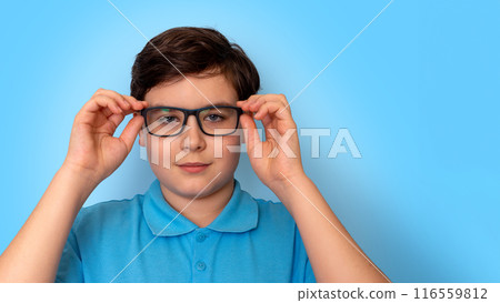 Close up of dark haired boy in glasses on light-blue background, look at camera 116559812