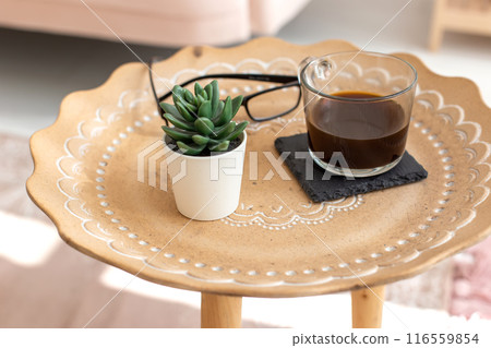 A succulent and a cup of black coffee stand on a small ceramic coffee table, with oriental ornaments 116559854