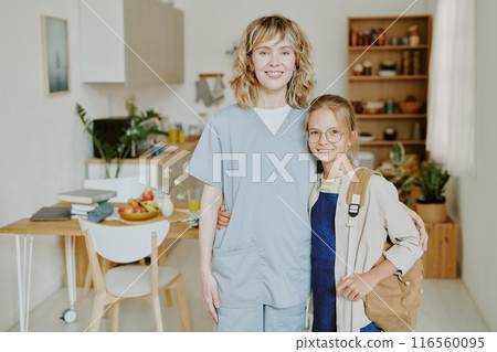 Young nurse Caucasian mom hugging her daughter while they sitting for photo in kitchen zone 116560095