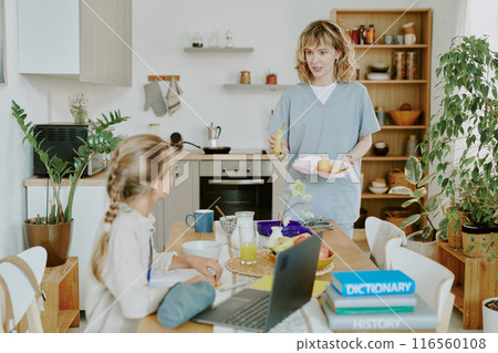 Blonde paramedic Caucasian mother discussing lunch food with her daughter who sitting at dining table and preparing for school Blonde paramedic Caucasian mother discussing lunch food with her daughter who sitting at dining table and preparing for school 116560108