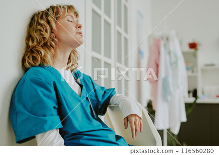 Tired Caucasian nurse taking nap while sitting on plastic chair after complicated shift at clinic 116560280