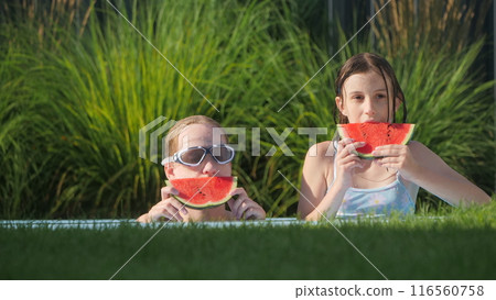 Two teenage girls enjoying watermelon by the edge of a backyard pool. 116560758