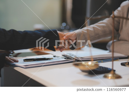 Lawyer shaking hands with a client making about documents, contracts, agreements, cooperation agreements with a female client at the lawyer's desk and a hammer at the table. 116560977