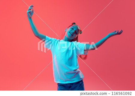 Portrait of young girl in white t-shirt and jeans spreading hands in positive expression against pink background in neon light Portrait of young girl in white t-shirt and jeans spreading hands in positive expression against pink background in neon light 116561092