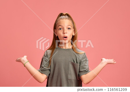 Emotive little girl in casual clothes, grey t0shirt standing with shocked face and spreading hands in surprise against peach background Emotive little girl in casual clothes, grey t0shirt standing with shocked face and spreading hands in surprise against peach background 116561209