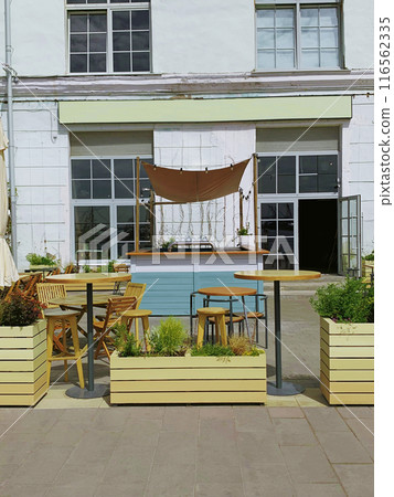 An inviting outdoor seating area with wooden furniture, planter boxes, and a canopy. Area for dining and relaxation at a cafe or restaurant.  116562335