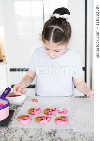 With focused attention, this budding culinary artist dips pretzels into a pot of melted chocolate, creating sweet delights in the warmth of a well-lit home kitchen. 116562397