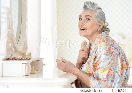 Smiling senior woman doing makeup in front of mirror at home 116562963