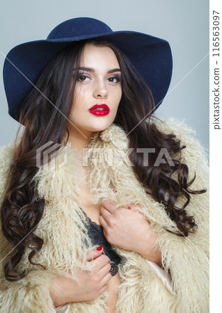 Gorgeous young brunette lady with makeup and long curly hair posing on blue background 116563097