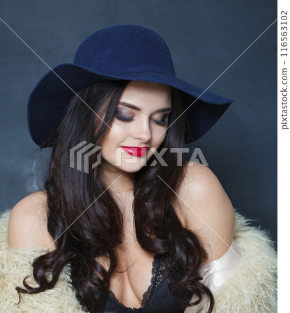 Cute young brunette lady with makeup and long curly hair posing on blue background, 116563102