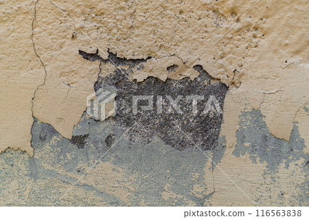 The wall of a concrete structure in which the layer of paint has worn out over time and cracked and in some places flew off, exposing the texture of the material. 116563838
