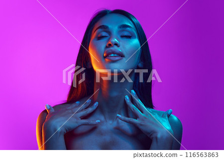 Femininity and sensuality. Attractive elegant young women with bare shoulders, long dark hair against purple background in neon light 116563863