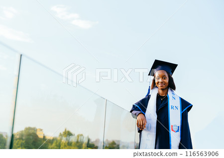 Portrait of African American graduate student n graduation gown and cap stand on rooftop with city view sunset light on background. Study, education, university, college, graduate concept. Portrait of African American graduate student n graduation gown and cap stand on rooftop with city view sunset light on background. Study, education, university, college, graduate concept. 116563906