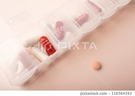 Pillbox with pills and supplements on pink background, top view. Capsules in daily organizer. Weekly pill organizer and pink pill. Clear plastic pill container and medications. High quality photo 116564393