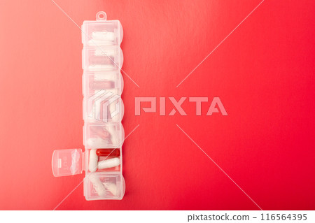 Pill organizer with pills and supplements on red background, top view. Capsules in daily pill box. Weekly pill organizer and pill. Clear plastic pill container and medications. High quality photo 116564395