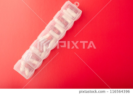 Pill organizer with pills and supplements on red background, top view. Capsules in daily pill box. Weekly pill organizer and pill. Clear plastic pill container and medications. High quality photo 116564396