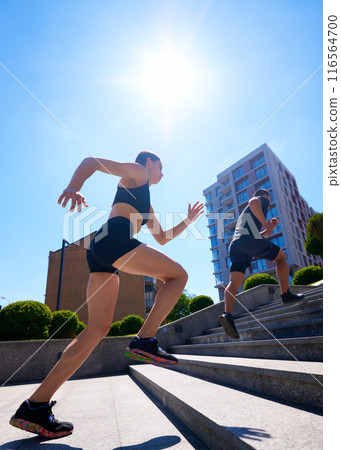Fit, young couple, man and woman, exercises by running up outdoor stairs in urban setting on bright, sunny day. Fit, young couple, man and woman, exercises by running up outdoor stairs in urban setting on bright, sunny day. 116564700