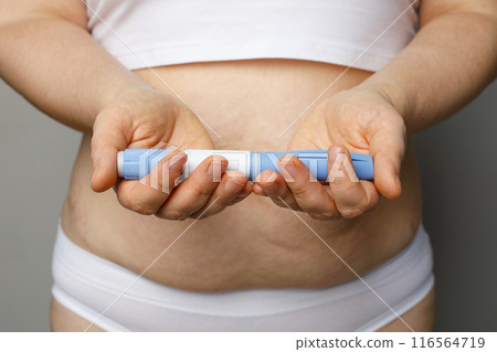 Injection pen in female hands indoor. Semaglutide or insulin drug against female belly. Semaglutide 116564719