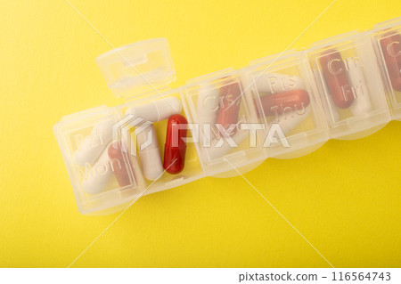 Pills organizer with supplements on yellow background, top view. Capsules in daily organizer. Weekly pillbox. Clear plastic pill container and medications. High quality photo Pills organizer with supplements on yellow background, top view. Capsules in daily organizer. Weekly pillbox. Clear plastic pill container and medications. High quality photo 116564743