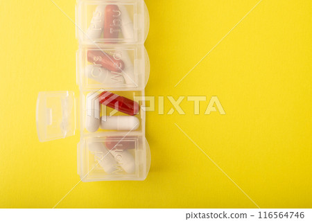 Pillbox closeup. Pills and supplements on yellow background, top view. Capsules in daily organizer. Weekly pill organizer and pill. Clear plastic pill container and medications. High quality photo 116564746