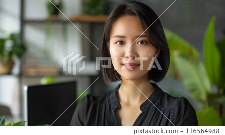 Young East Asian Woman Working in a Modern Home Office with Plants and Books in Background 116564988