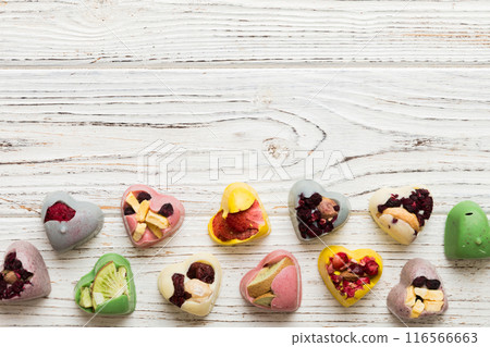 chocolate sweets in the form of a heart with fruits and nuts on a colored background. top view with space for text, holiday concept chocolate sweets in the form of a heart with fruits and nuts on a colored background. top view with space for text, holiday concept 116566663
