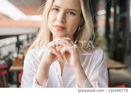 Close-up Portrait of beautiful young blonde woman in balcony cafeteria. Happy smiling female relaxing in a coffee shop. 116566778