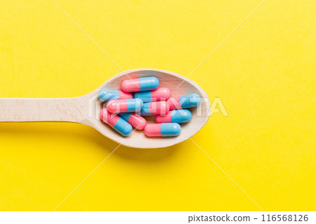 Vitamin capsules in a spoon on a colored background. Pills served as a healthy meal. Red soft gel vitamin supplement capsules on spoon 116568126