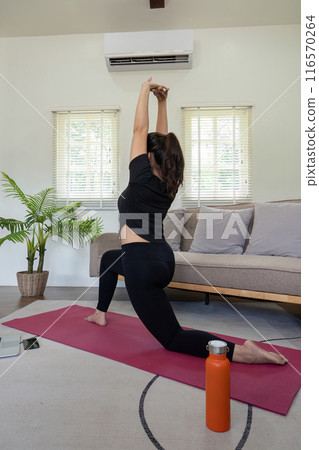 Woman Practicing Yoga Indoors on a Red Mat in a Modern Living Room with Natural Light and Green Plant Woman Practicing Yoga Indoors on a Red Mat in a Modern Living Room with Natural Light and Green Plant 116570264