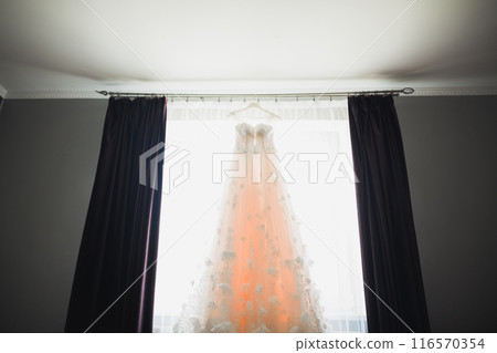 The perfect wedding dress with a full skirt on a hanger in the room of the bride 116570354