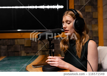 A woman is recording a podcast in a professional studio using a quality microphone A woman is recording a podcast in a professional studio using a quality microphone 116571549