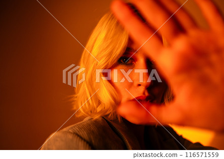 In cinematic lighting, a blonde woman poses elegantly, exuding beauty and emotion with raised hand 116571559