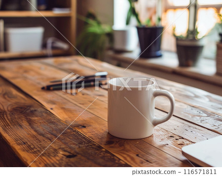 A white mug sitting on a vintage aged rosewood desk with various modern office supplies organized around it.  116571811