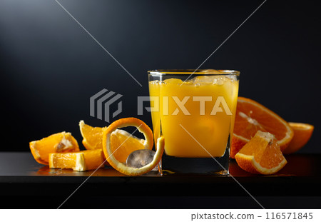 Glass of orange juice with ice on a black background. 116571845
