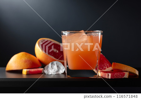 Glass of grapefruit juice with ice on a black background. 116571848
