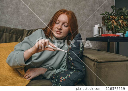 young woman checking her temperature, highlighting the personal responsibility of health management 116572339