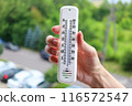 A womans hand with a plastic mercury thermometer shows high air temperature in Celsius outdoors in the shade. more than 36 degrees. 116572547