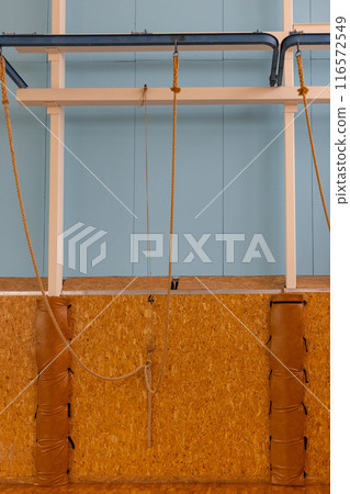 Indoor Climbing Wall with Ropes and Padding in Gymnasium for Fitness and Training. Indoor Climbing Wall with Ropes and Padding in Gymnasium for Fitness and Training. 116572549