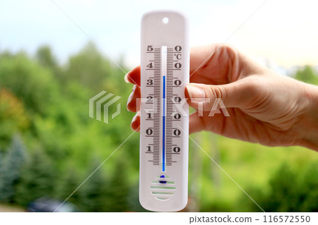 A womans hand with a plastic mercury thermometer shows high air temperature in Celsius outdoors in the shade. more than 36 degrees. 116572550