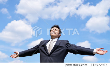 A businessman stretching with his arms outstretched under the blue sky 116572913