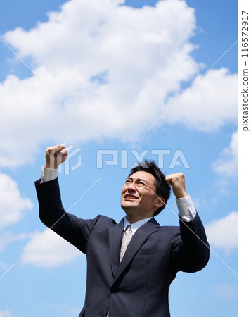 A man in a suit doing a fist pump under the blue sky A man in a suit doing a fist pump under the blue sky 116572917