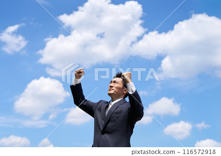 A man in a suit doing a fist pump under the blue sky 116572918
