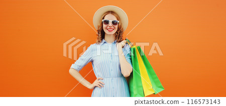Fashion, clothing. Stylish beautiful happy woman with colorful shopping bags in summer hat on orange 116573143