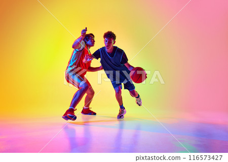 Two players, focused and energetic, engage in rigorous basketball training session in neon light against gradient studio background. 116573427