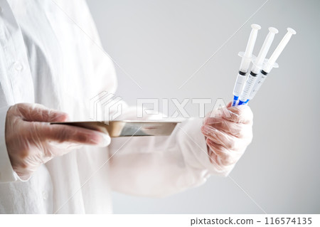 The doctor's hands in a white coat and gloves hold three syringes with medicine. 116574135