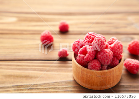 Ripe raspberries in wooden bowl on brown background. Top view Ripe raspberries in wooden bowl on brown background. Top view 116575056
