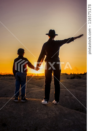 A woman and a child look at the sunset holding hands. The concept of family, childhood. Beautiful landscapes and peace A woman and a child look at the sunset holding hands. The concept of family, childhood. Beautiful landscapes and peace 116575178
