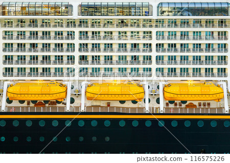 Side view of three yellow lifeboats and balconies on a large cruise ship, ship safety equipment 116575226
