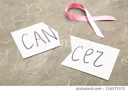 Scissors cutting a piece of paper with Cancer word with pink ribbon. Breast cancer awareness symbol. 116575372