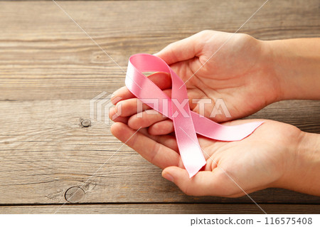 Hands holding breast cancer ribbon. Pink ribbon on grey wooden background Hands holding breast cancer ribbon. Pink ribbon on grey wooden background 116575408
